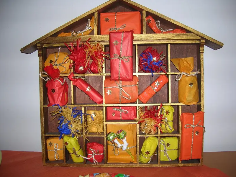 A homemade wooden advent calendar shaped like a house, its compartments filled with small wrapped parcels