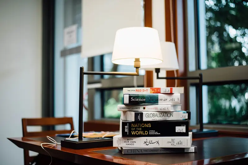 A stack of books on a table under a reading lamp