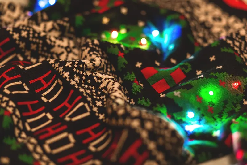 A knitted Christmas jumper with a festive pattern among fairy lights