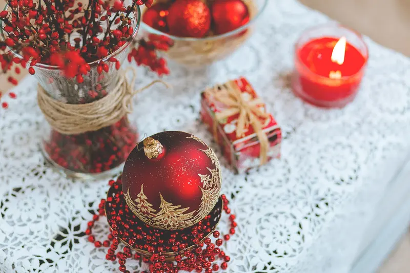 A table decorated for Christmas with red baubles, a candle and a small present on a white lace cloth