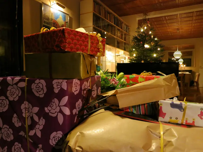A pile of wrapped presents beside a lit Christmas tree