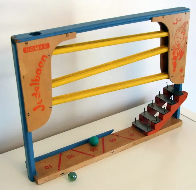 A vintage wooden marble run with yellow rails and steps, and green marbles at the bottom