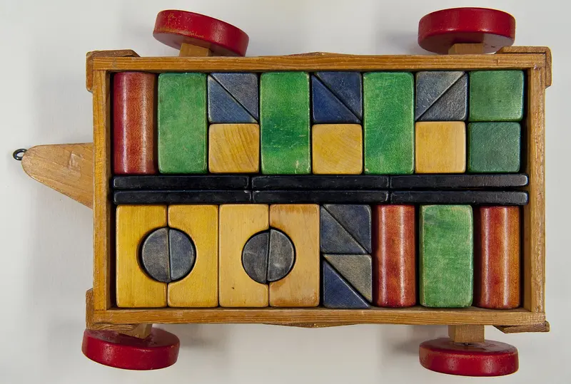 A wooden cart on red wheels packed with painted wooden building blocks
