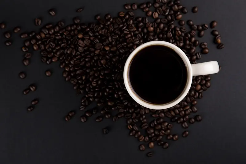 A cup of black coffee seen from above, surrounded by roasted coffee beans
