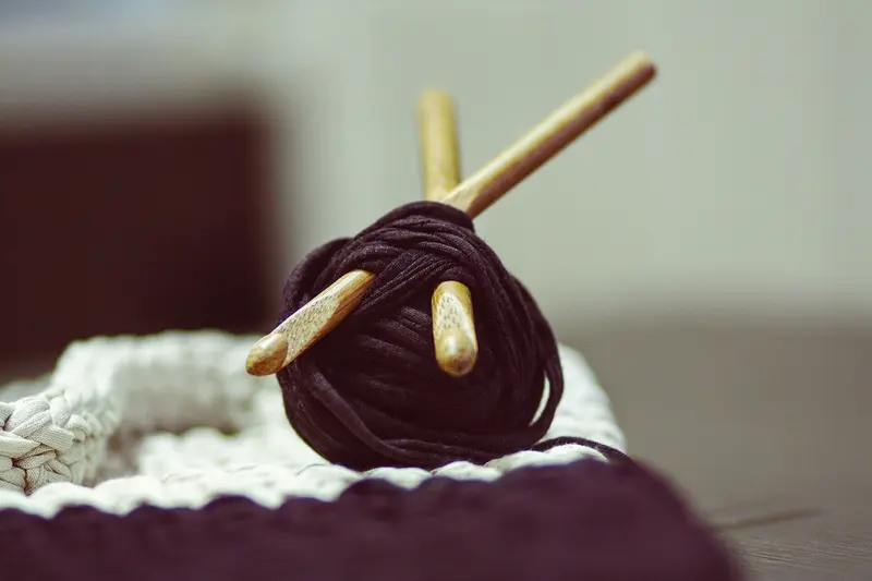 A ball of dark yarn with two wooden knitting needles pushed through it