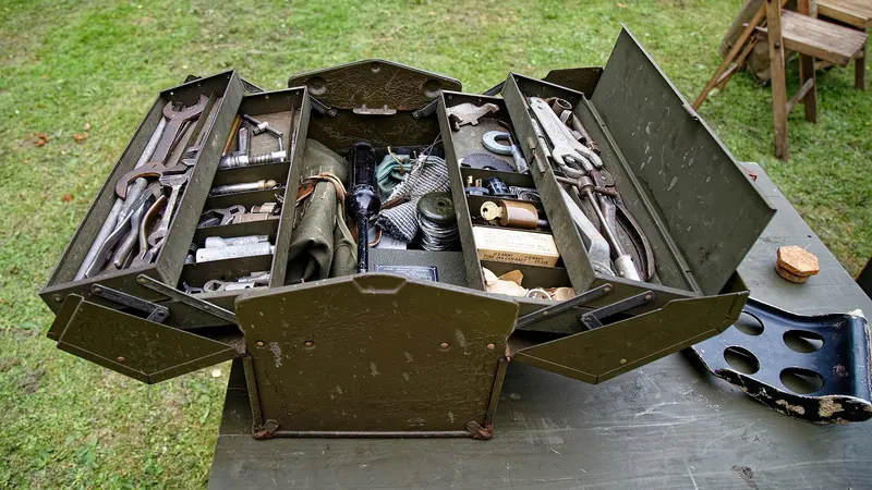 An open metal toolbox full of old hand tools on a garden table