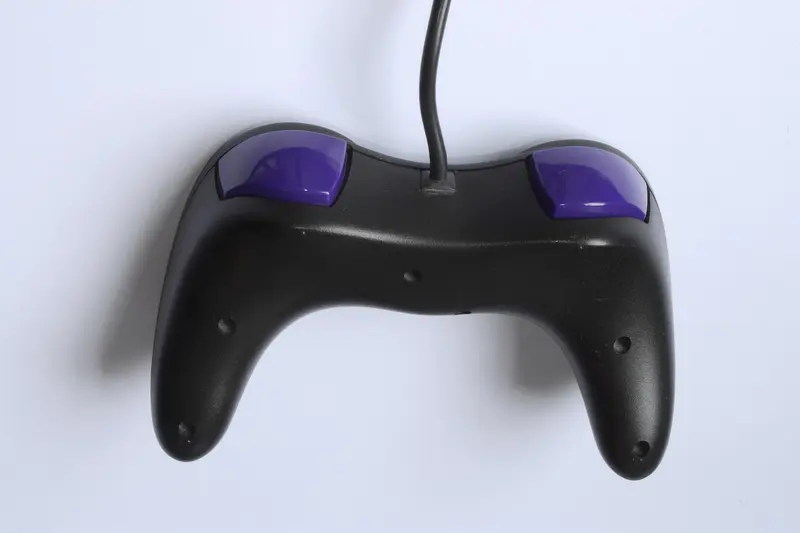 A black game controller with purple shoulder buttons on a white background
