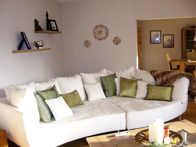 A white sofa with green cushions and a candle on the coffee table