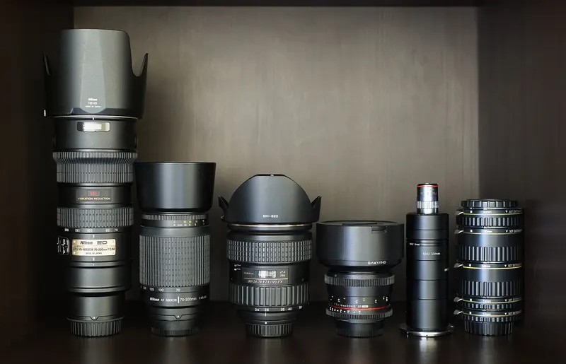 A row of camera lenses and extension tubes on a wooden shelf