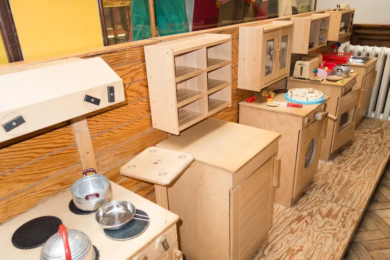 A row of wooden toy kitchens with little pans and cupboards
