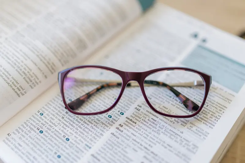 A pair of purple reading glasses resting on an open book