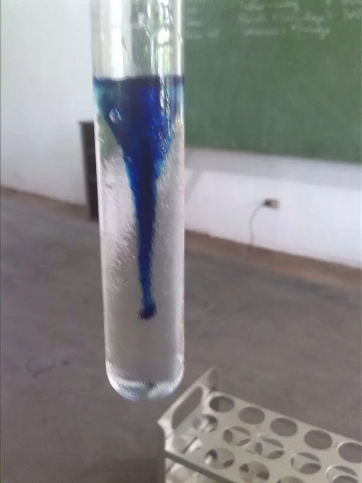 Blue dye spreading through water in a test tube, with a test-tube rack behind