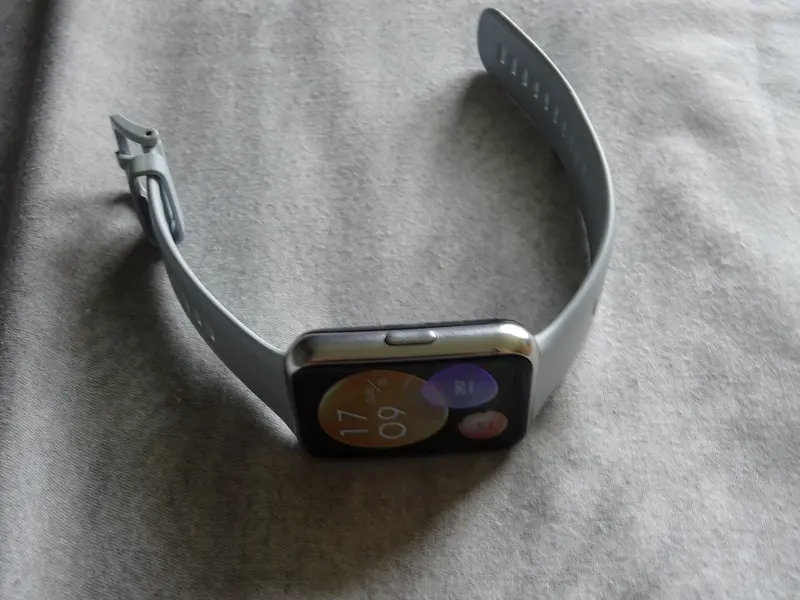 A smartwatch with a grey strap lying on a soft fabric