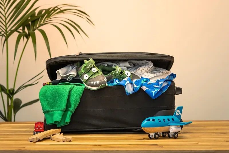 An open suitcase overflowing with clothes, with a toy aeroplane beside it